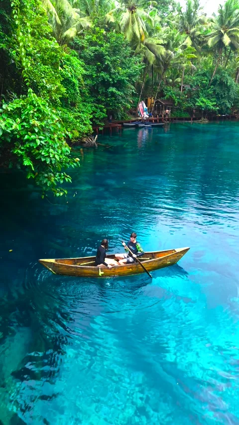 Aerial view of a young man and a young woman paddling a wooden boat on clear Stock Footage 346361173