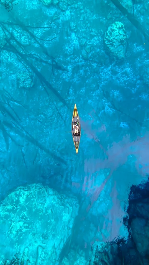 Aerial view of a young man and young woman paddling a wooden canoe in clear Stock Footage 346361511