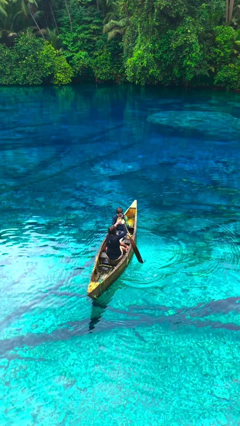 Aerial view of a young man and a young woman paddling a wooden canoe on clear Stock Footage 346747973