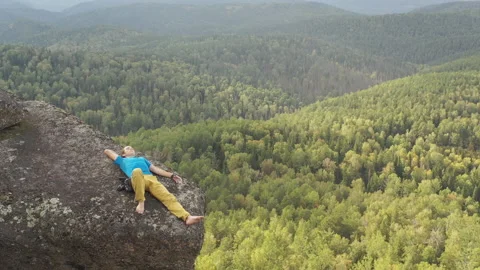 Aerial view of a young man lying on the edge of a cliff with his eyes closed. Stock Footage 149083773