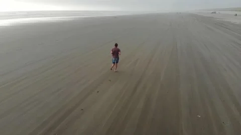 Aerial view of young man running jogging on wide beach during day Stock Footage 143424029