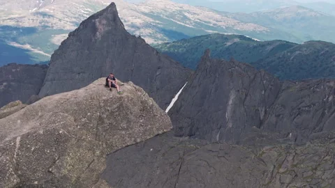 Aerial view of a young man sitting on top of a rocky mountain and drinking beer Stock Footage 278324565