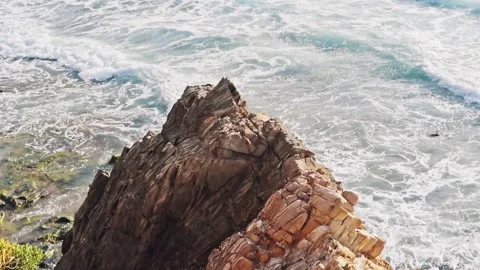 Aerial viewpoint capturing a large, textured ocean rock surrounded by waves Stock Footage 345044518