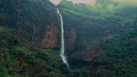 Aerial waterfall cascading down rocky cliff surrounded by green forest Stock Footage 339780938