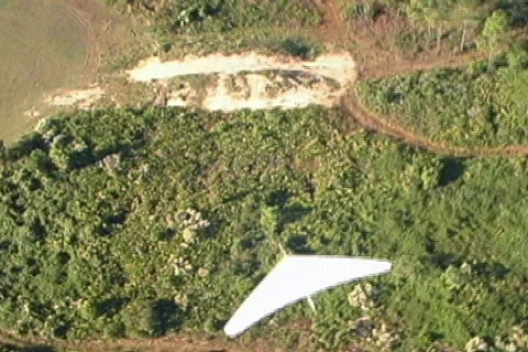 Aerial of White Hang Glider Flies In and Out of Frame Over Land Stock Footage