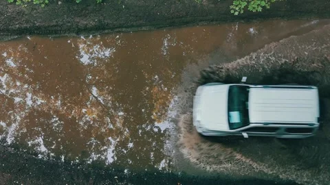 Aerial of a white SUV driving through muddy water on rugged terrain. Видео 341894256
