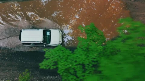 Aerial of a white SUV driving through muddy water on rugged terrain. Stock Footage 341894258