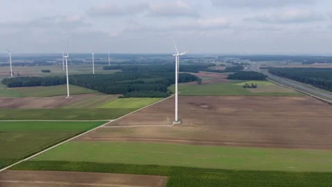Aerial wind farm over fields, forest block, and parallel highway Stock Footage 327094368