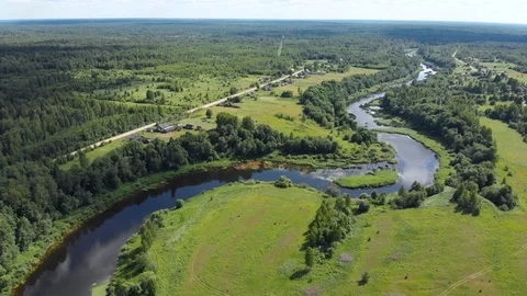 Aerial of winding river between green meadow forest with distant village Russia Stock Footage 116864761