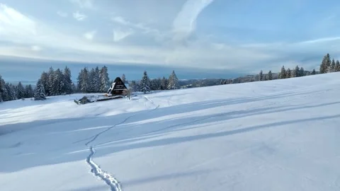 Aerial winter drone flight towards wooden chalet on snowy mountain meadow Stock Footage 336384435