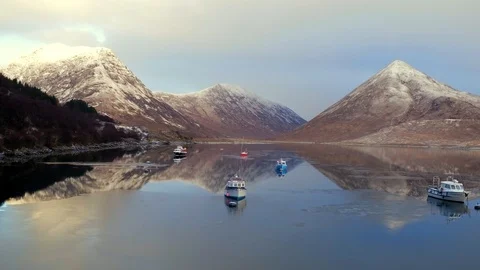 Aerial: Winter mountain reflections on mirror flat icy water with boats. 4K Stock Footage 88877265