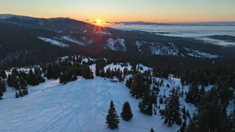 Aerial winter orbit showing sunrise behind distant mountain peaks Stock Footage 336445864