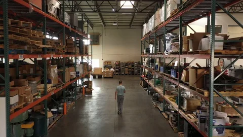 Aerial of worker walking down row of warehouse shelves Stock Footage 129979814