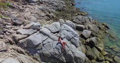 Aerial: Young lady is posing on the rocks on the wild beach. Thailand. Phuket. Stock Footage 76726692