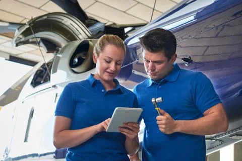Aero Engineer And Apprentice Working On Helicopter In Hangar Looking At Digit Stock Photos