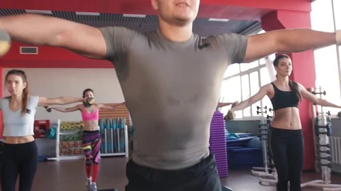 Aerobics class stepping together led by instructor and lifting dumbbells at the Видео 75869538