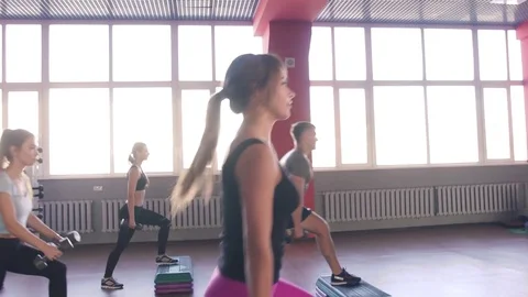 Aerobics class stepping together led by instructor and lifting dumbbells at the Stock-Footage 75869601