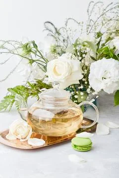 Aesthetic table setting. Green tea teapot, macaroon desserts, white roses and Stock Photos