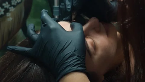 Aesthetician's gloved hands applying microblading pigment to a woman's eyebrows, Stock Footage 332058039