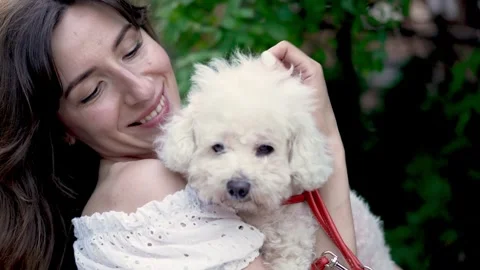 Affectionate brunette cuddling a cute white poodle outdoors Stock Footage 245714806