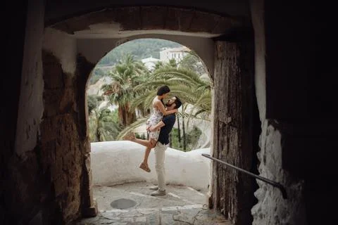 Affectionate couple embracing while standing on street in old arch of tropical t Stock Photos