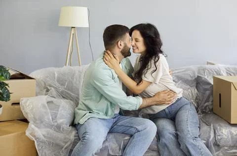 Affectionate couple hugging on covered sofa with boxes, excited for new home Stock-Fotos