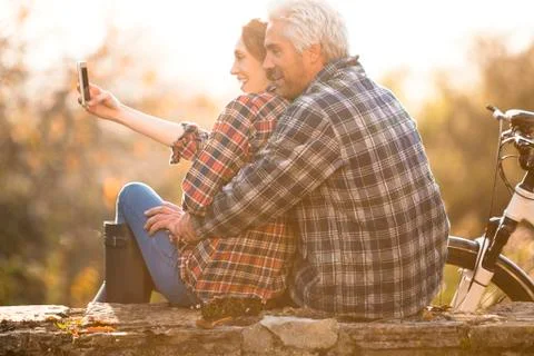 Affectionate couple hugging taking selfie with camera phone in autumn park Stock Photos