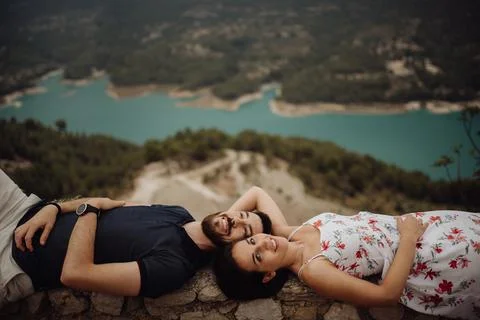 Affectionate couple resting while lying on stone fence in mountains Foto stock