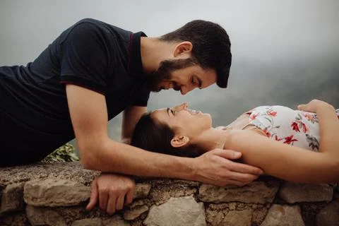 Affectionate couple resting while lying on stone fence in mountains 写真素材