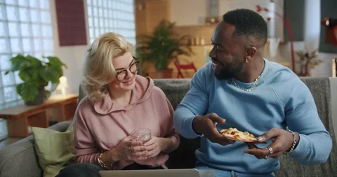 Affectionate couple sharing tasty slice of pizza chilling on cozy gray sofa in Stock Footage 123672277