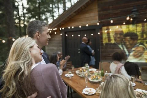 Affectionate couple watching projected slideshow at anniversary party on cabin b Foto stock