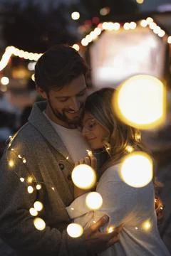 Affectionate couple wrapped in string lights at movie in the park Stock Photos