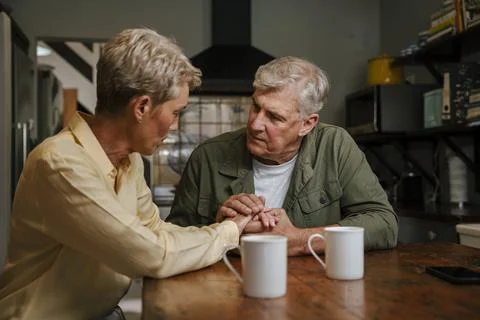 Affectionate elderly couple holding hands in kitchen Stock Photos
