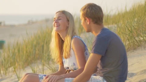 Affectionate hipster couple having a conversation while sitting in the dunes Stock Footage 73782311