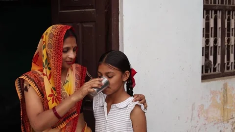 Affectionate Indian mother helping young daughter drink water or milk from .. Stock Footage 335119442