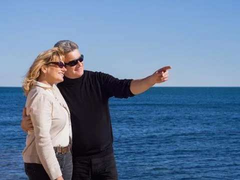 Affectionate mature couple at the seaside pointing copyspace Stock Photos