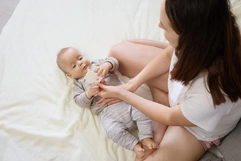 Affectionate mother sitting on bed playing with her adorable newborn son wi.. Stock Photos
