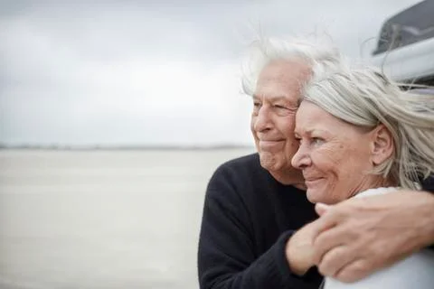 Affectionate senior couple hugging and looking away on beach Stock Photos