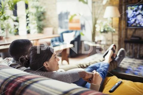 Affectionate young couple watching TV on living room sofa Stock Photos