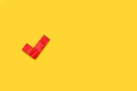 Affirmative check mark made with red wooden blocks on a yellow background Foto stock