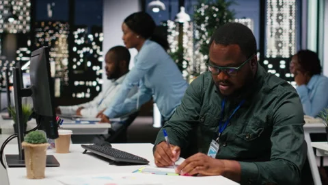 African american advisor extracting data by hand on a notebook late at night Stock Footage 318562518