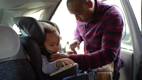 African American bald dad checking belts on child car seat Video stock 133552512