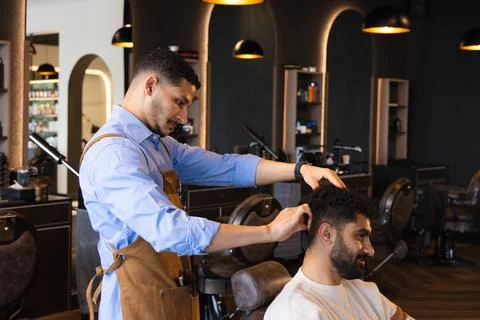 African American barber and client, wearing leather apron styling hair, client Stock Photos