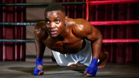 African american boxer practicing push ups on boxing ring inside gym Stock Footage 241322004