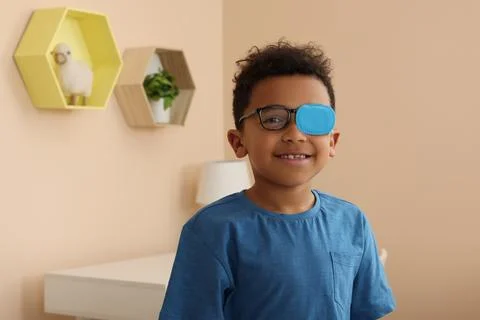 African American boy with eye patch on glasses in room, space for text. Str.. Stock Photos