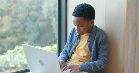 African American boy pausing at rain-speckled window then typing homework on Video stock 344253584