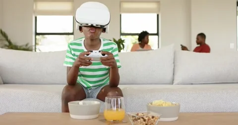 African American boy playing VR game holding controller on sofa while parents Stock Footage 340069386