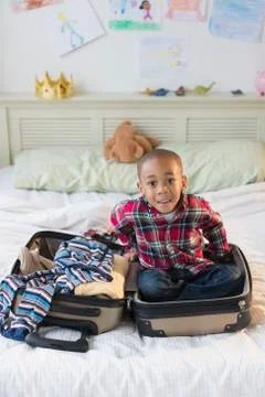 African American boy sitting in suitcase on bed Stock Photos