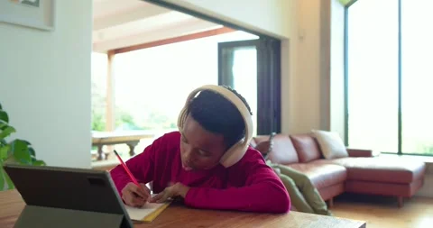 African American boy tapping tablet to study and writing in notebook at home Stock Footage 344644481