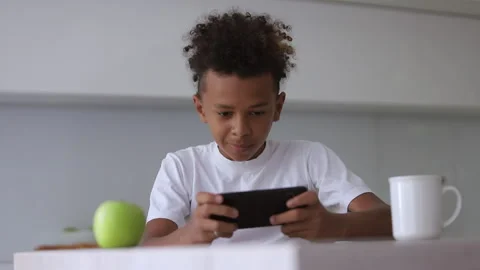 African American boy is using smartphone while sitting at table in apartment Stock Footage 136652102